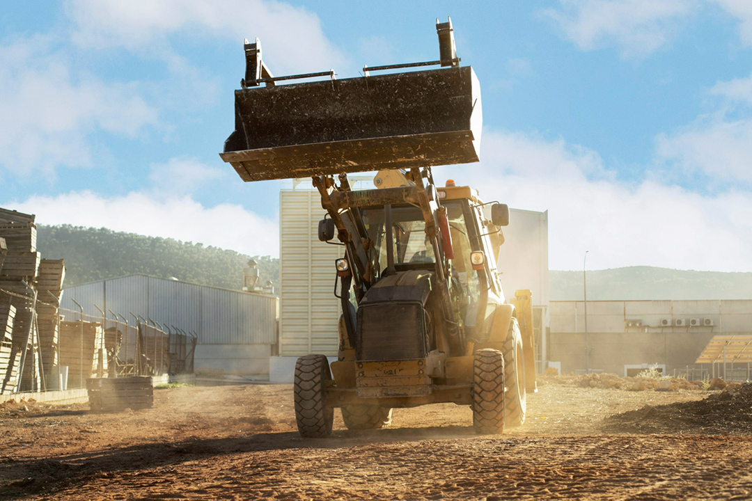 Dust-suppressants-for-mining-and-cosntruction-1 A TLB with its front scoop raised on a dusty construction site, hinting to the need for dust suppressants.