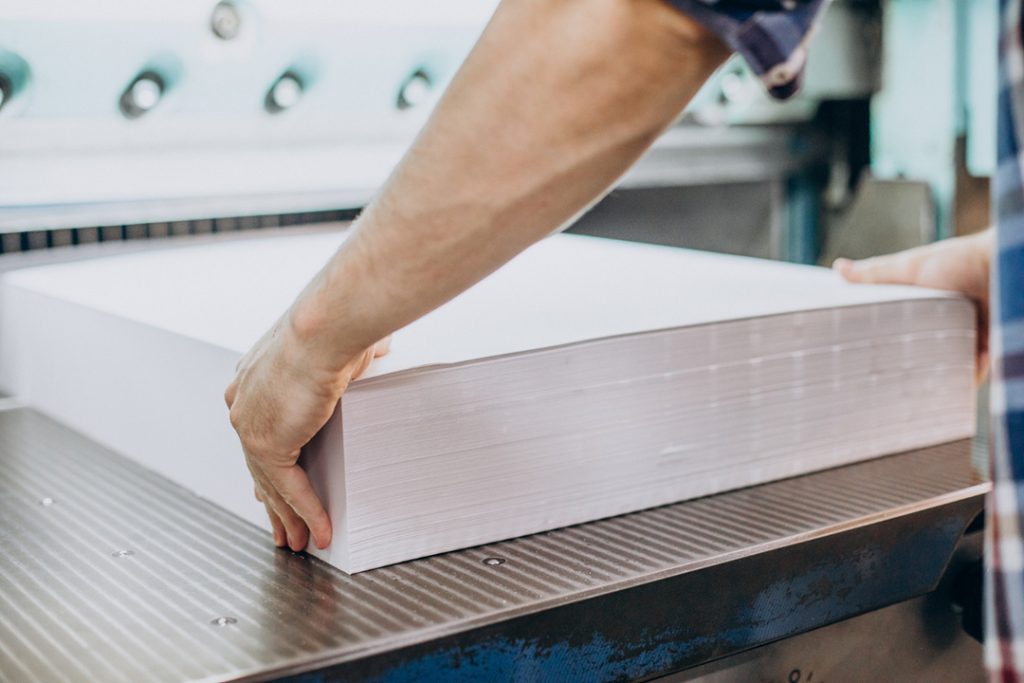 A factory worker lines up a stack of paper on an industrial guillotine.