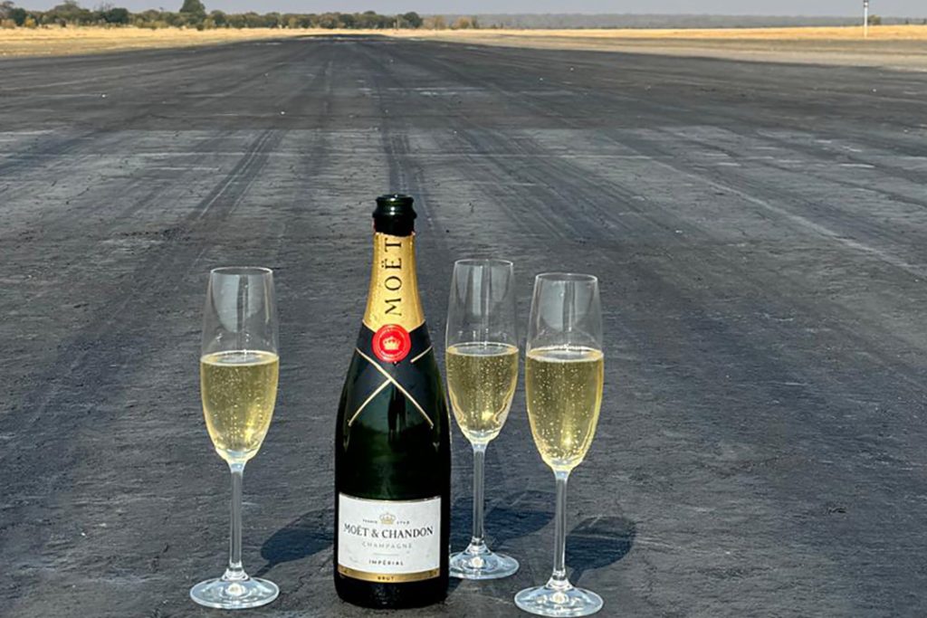 Three champagne flutes and a bottle of Moet sitting on a dirt airstrip that has been commissioned.